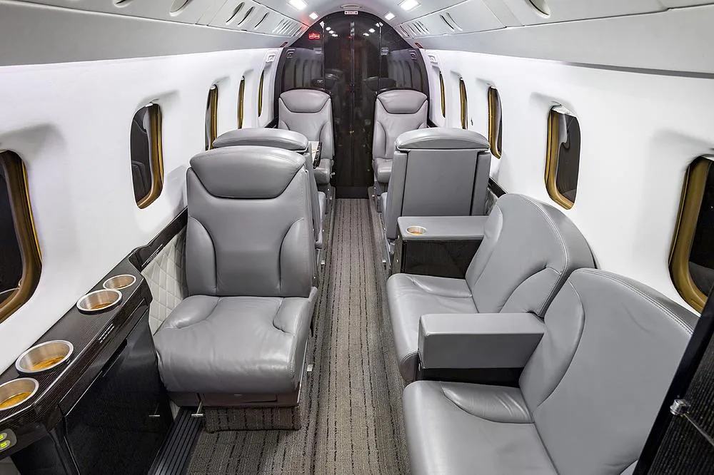 A view down the aisle of a business jet cabin with gray leather seats and dark wood accents.