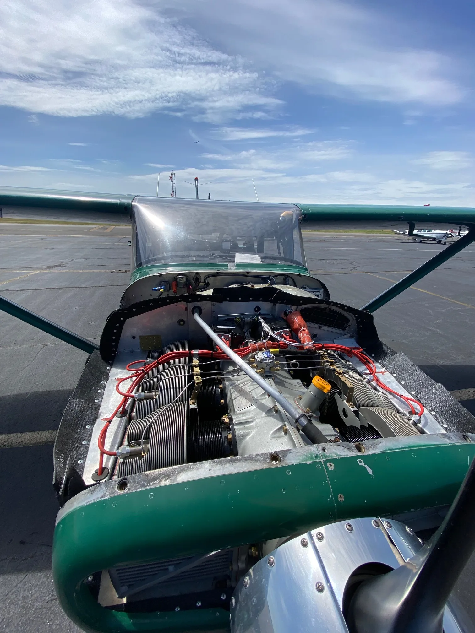 Front view of a green Cessna 210 aircraft with the engine cowling open, revealing the engine.