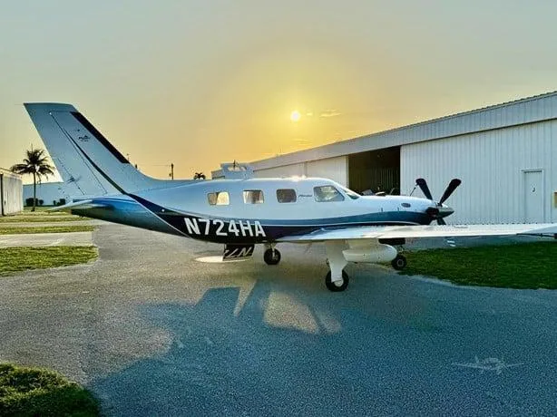 The white and blue Piper M500 (Meridian) aircraft, registration N724HA, parked outside a hangar at sunset.