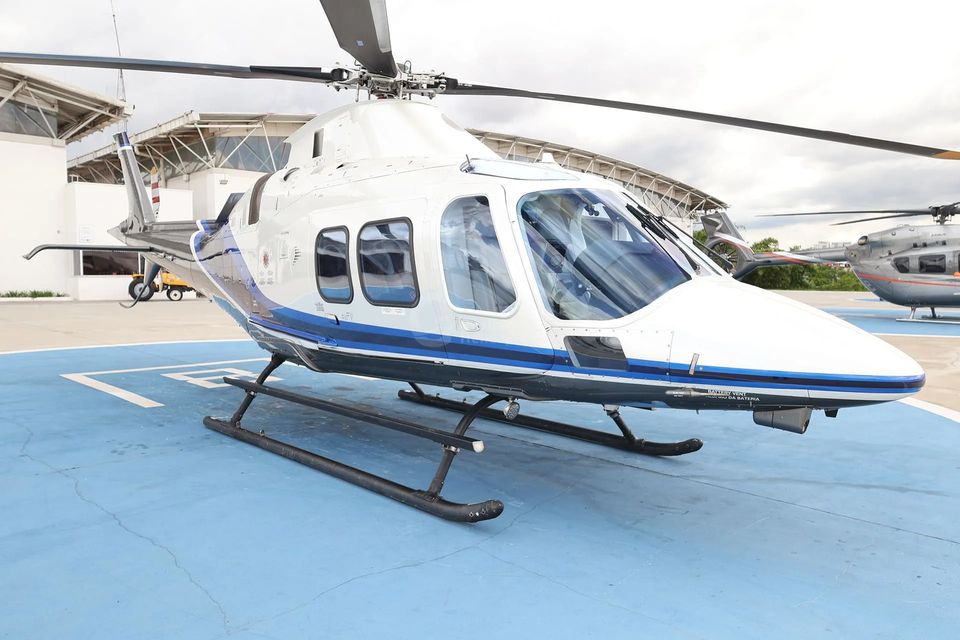 A close-up front view of a white and blue helicopter parked on a blue helipad.