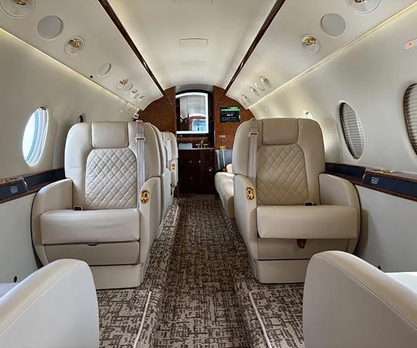 A wider view of the private jet's cabin, featuring beige quilted seats and a galley area at the rear.
