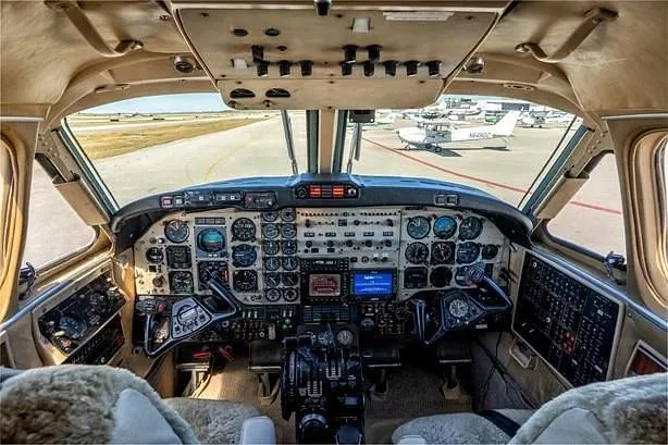 The cockpit of a turboprop aircraft with a complex instrument panel and a view of the airport runway outside.