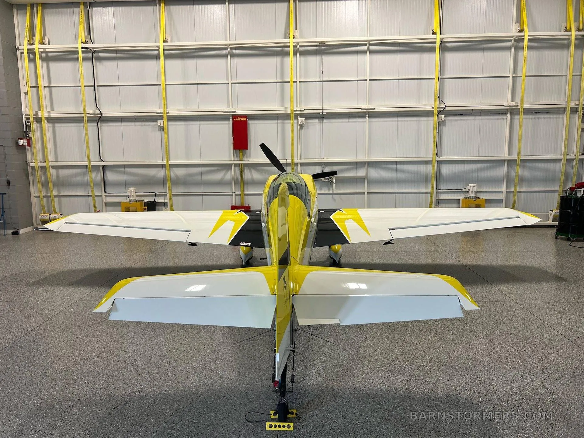 A yellow and white Extra 330LT aerobatic aircraft with registration N326LT, viewed from directly behind in a hangar.