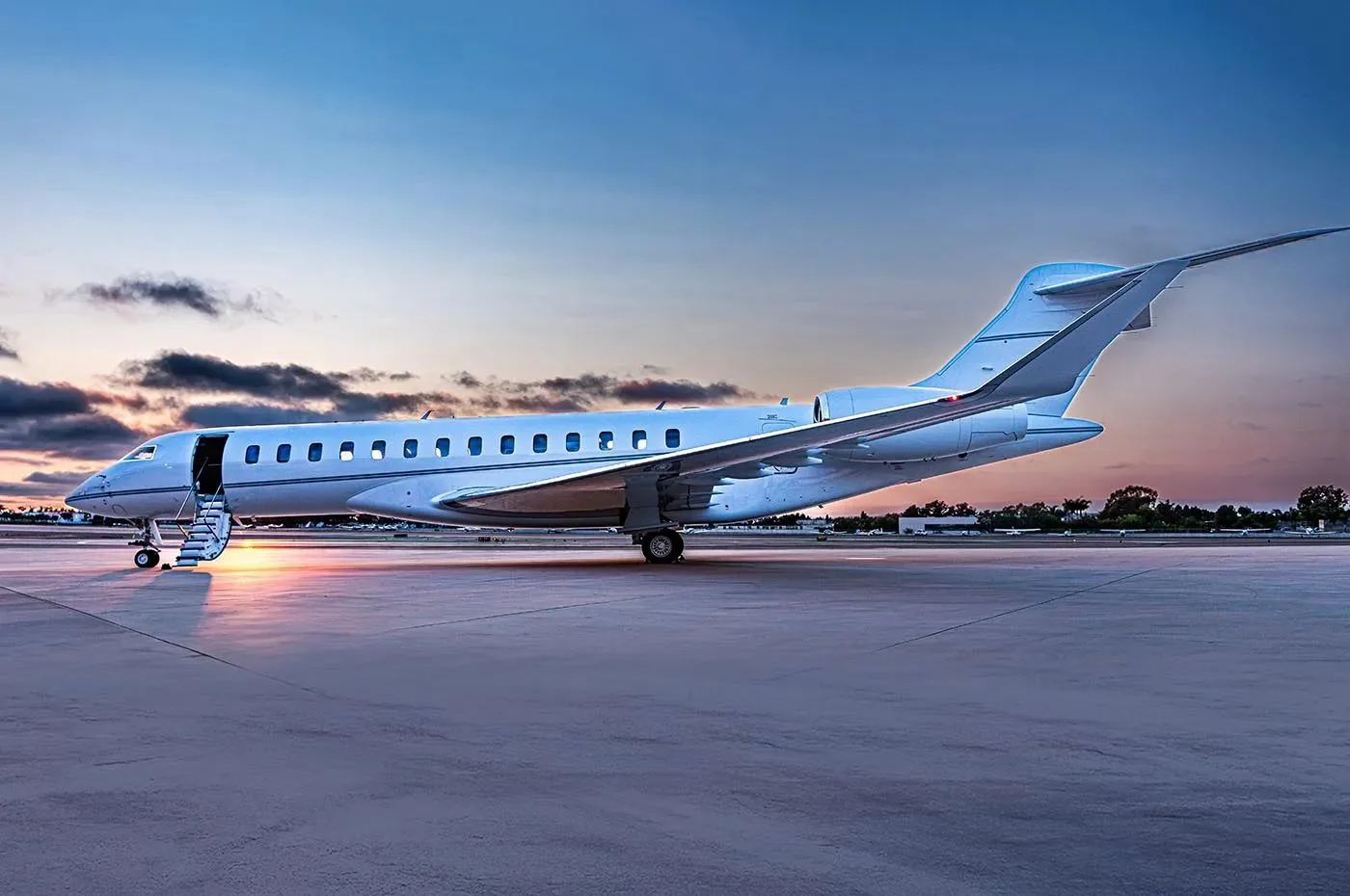 A white business jet with its door open and stairs extended, parked on a tarmac at sunset.