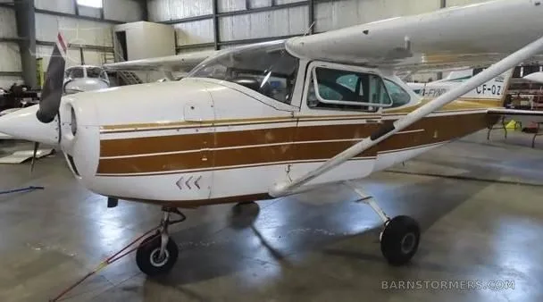 A white and gold Cessna 172 parked in a hangar, viewed from the front-left.