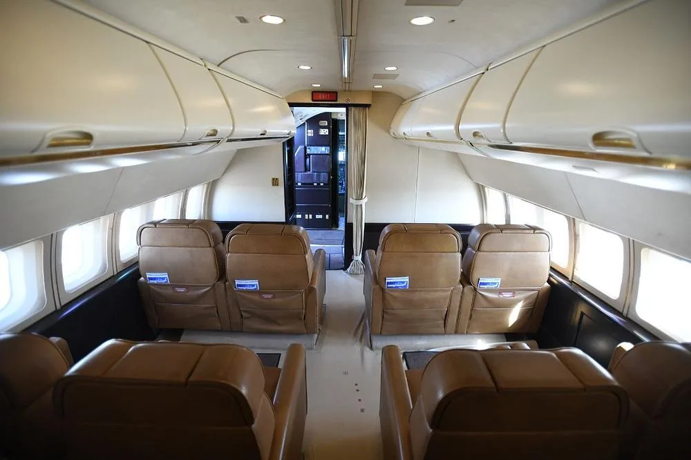 A view of the aircraft cabin from the front, showing tan leather seats and overhead bins.
