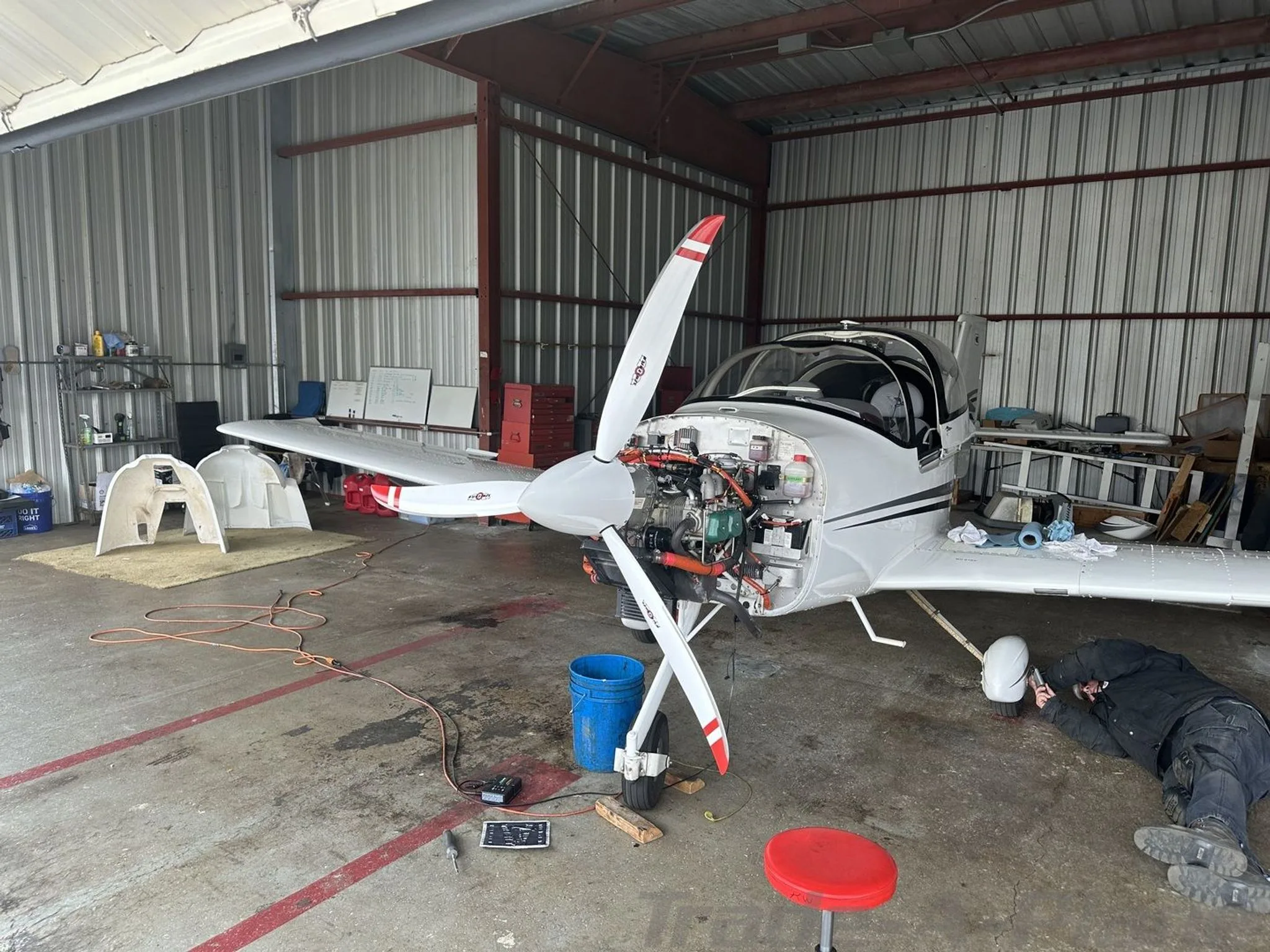 A white Tecnam P2002 Sierra aircraft in a hangar with its engine cowling removed for maintenance.