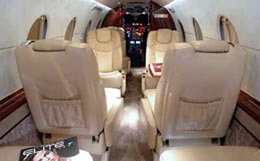 The interior of a jet aircraft is shown with cream-colored leather seats and wood trim.