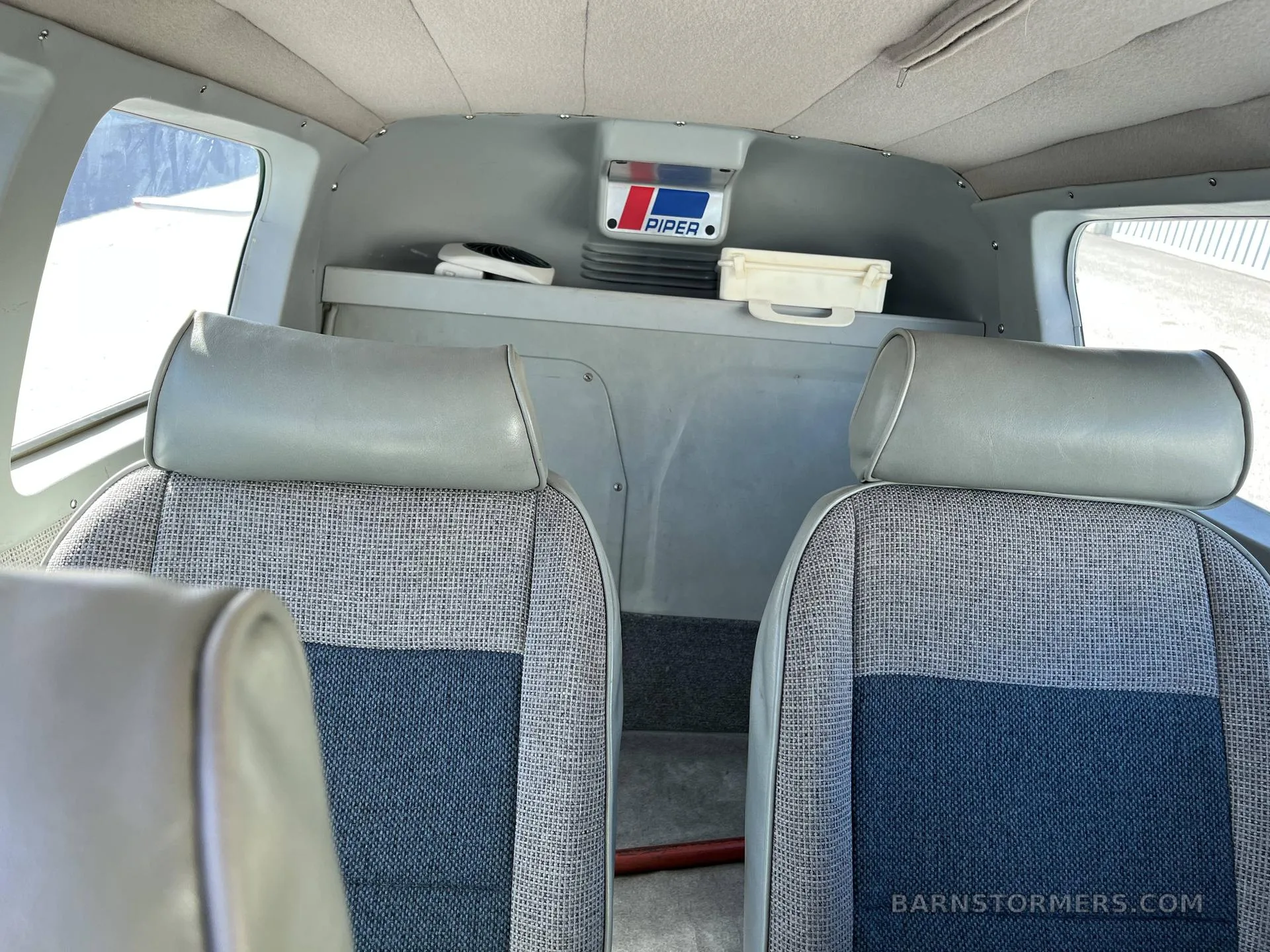 The aircraft's cabin features two grey and blue patterned seats with a Piper logo visible on the rear bulkhead.
