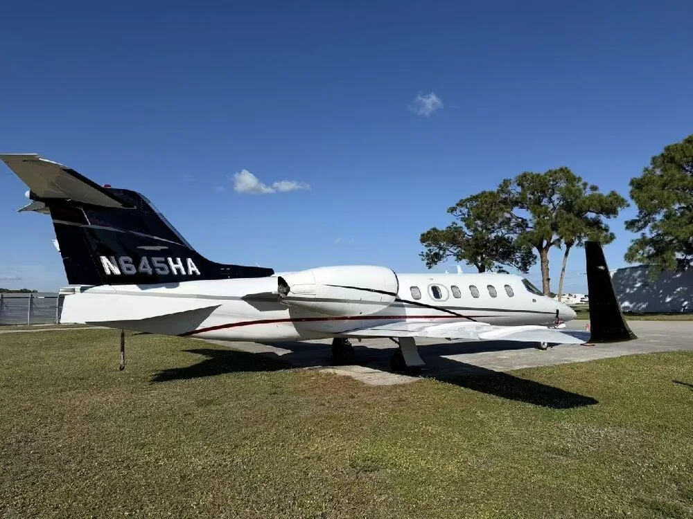 A side view of the white Learjet 35A N645HA with a black tail, parked on grass next to an asphalt ramp.