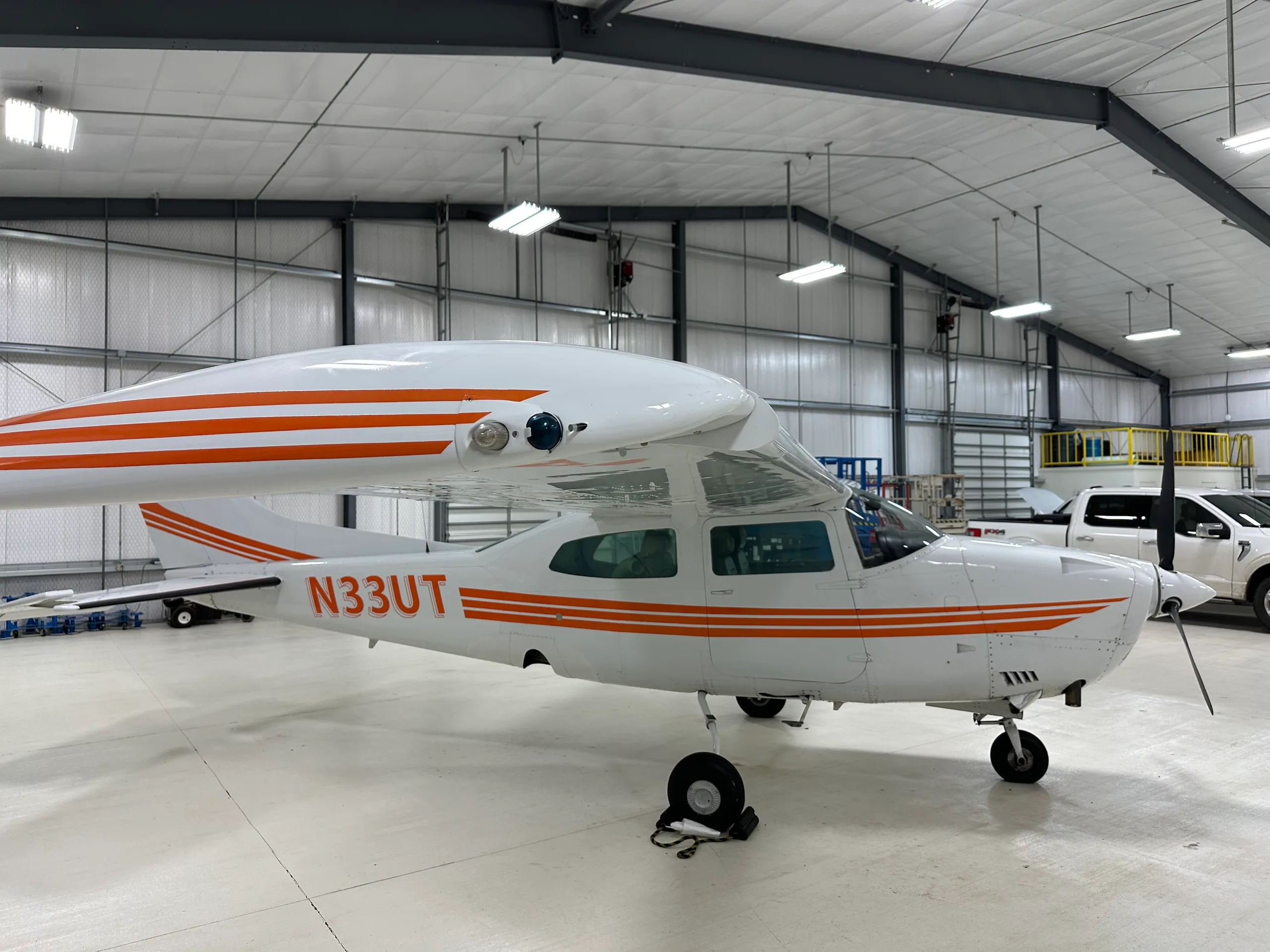 A Cessna 206 Stationair aircraft with orange stripes parked in a hangar.