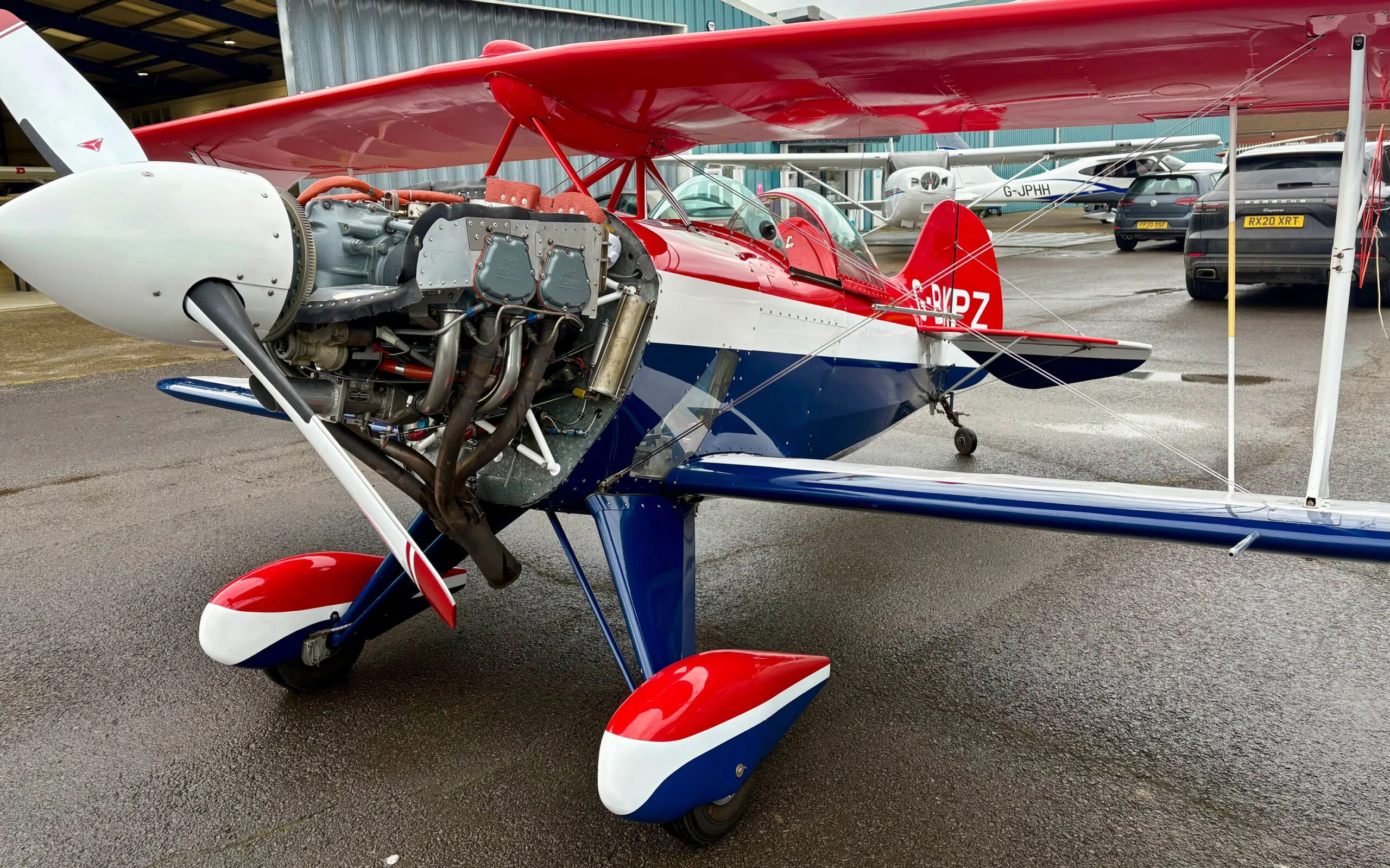 A red, white, and blue Pitts S1T biplane with its engine cowling open, revealing the engine.