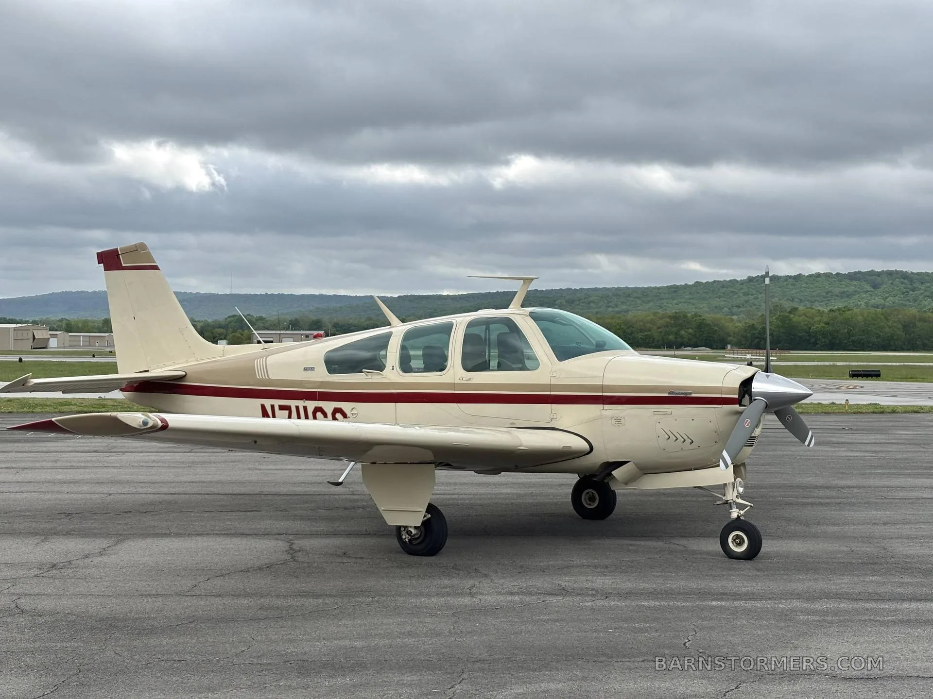 A full side view of the cream and red Beechcraft Debonair N711GS parked on an asphalt ramp.