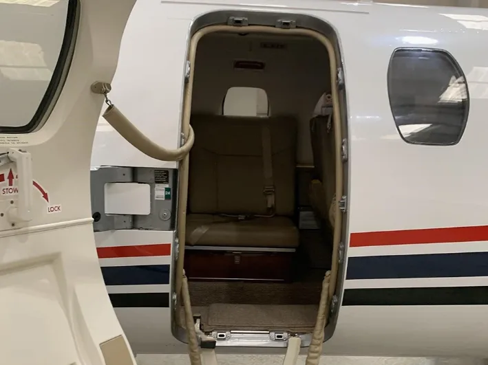 A close-up view of the open private jet door, showing the first tan leather seat and the steps leading into the cabin.