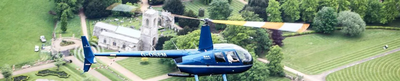 A blue helicopter flies over a church and green fields.