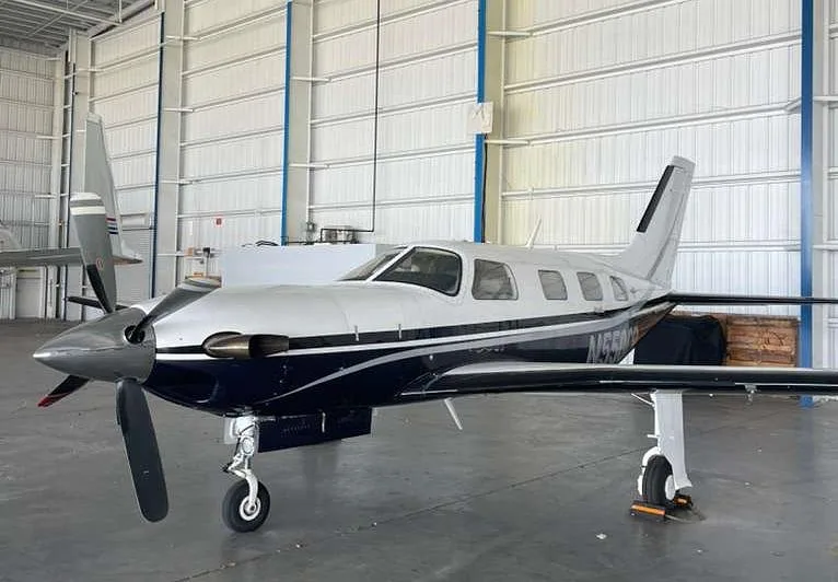 A front-side view of the Piper M500 aircraft N550CR, showing its propeller and silver and dark blue livery, inside a hangar.
