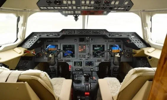 The cockpit of a business jet with multiple digital displays and beige leather seats.