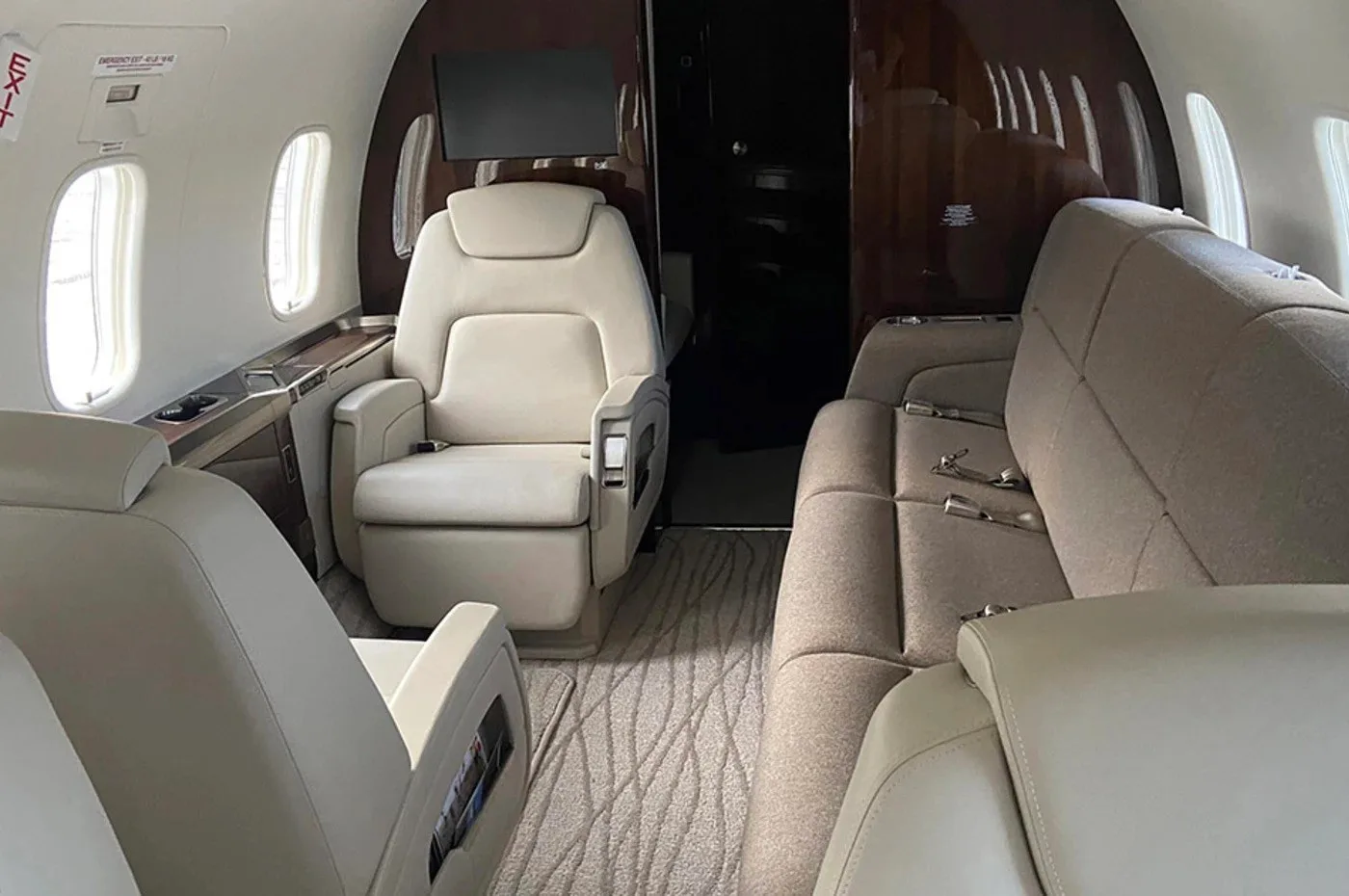 A view inside a private jet cabin, featuring a single beige armchair and a brown fabric sofa, with dark wood paneling.