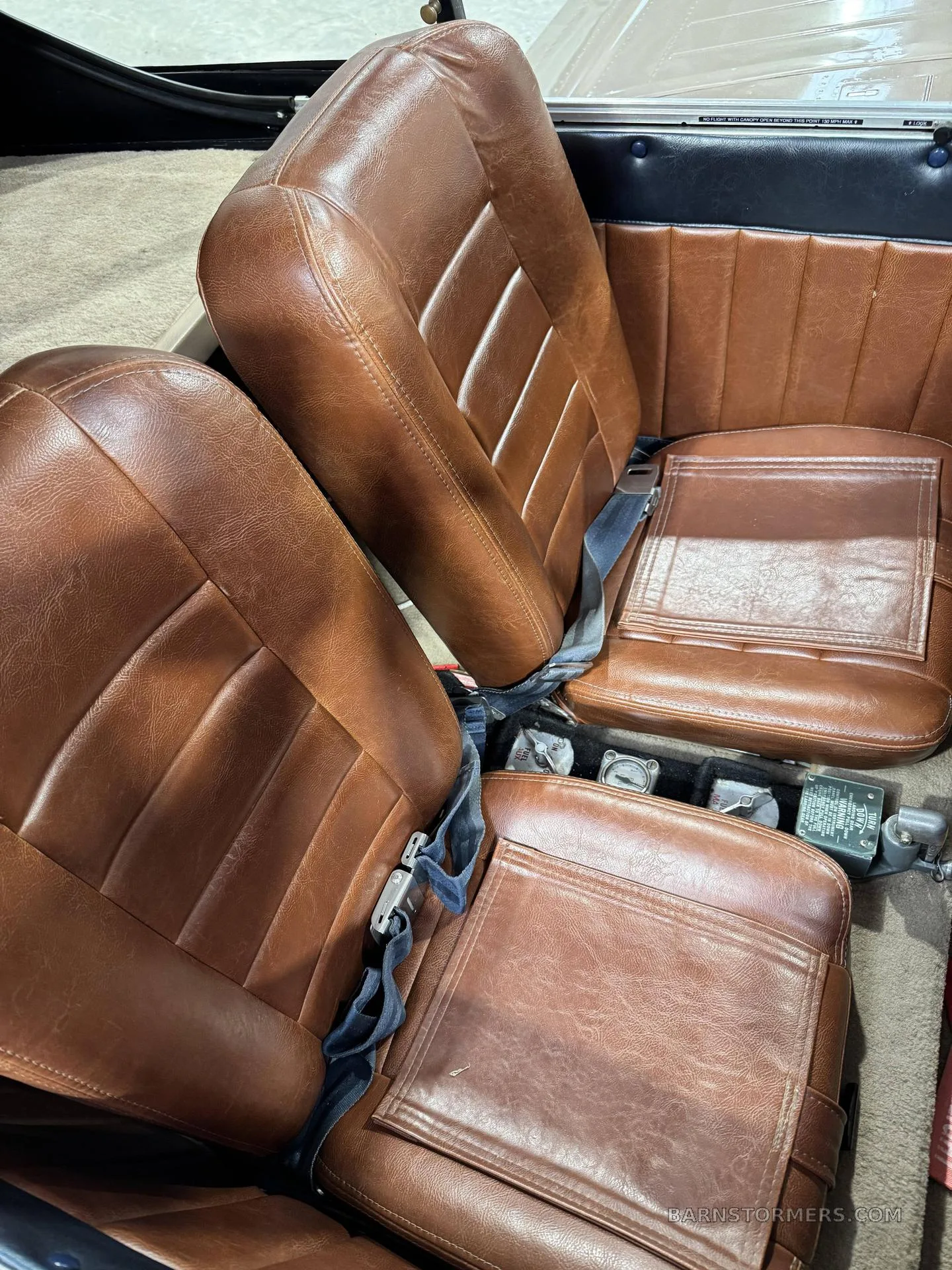 Brown leather aircraft seats with blue seatbelts in a small cabin.