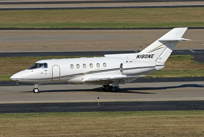 A white business jet with black and gold stripes, tail number N180NE, on an airport tarmac.