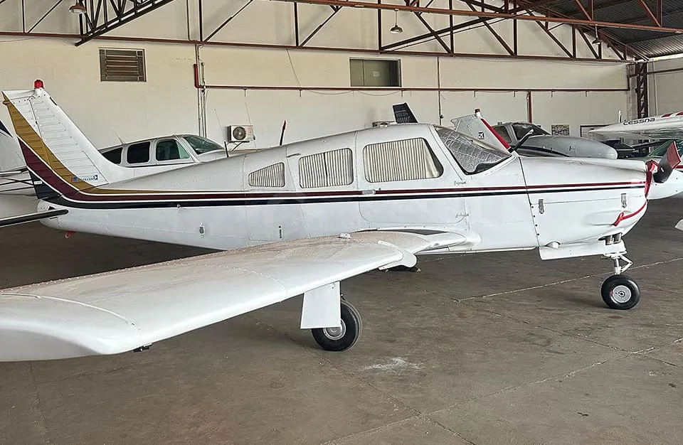 A white single-engine propeller aircraft with black and gold stripes is parked inside a hangar.