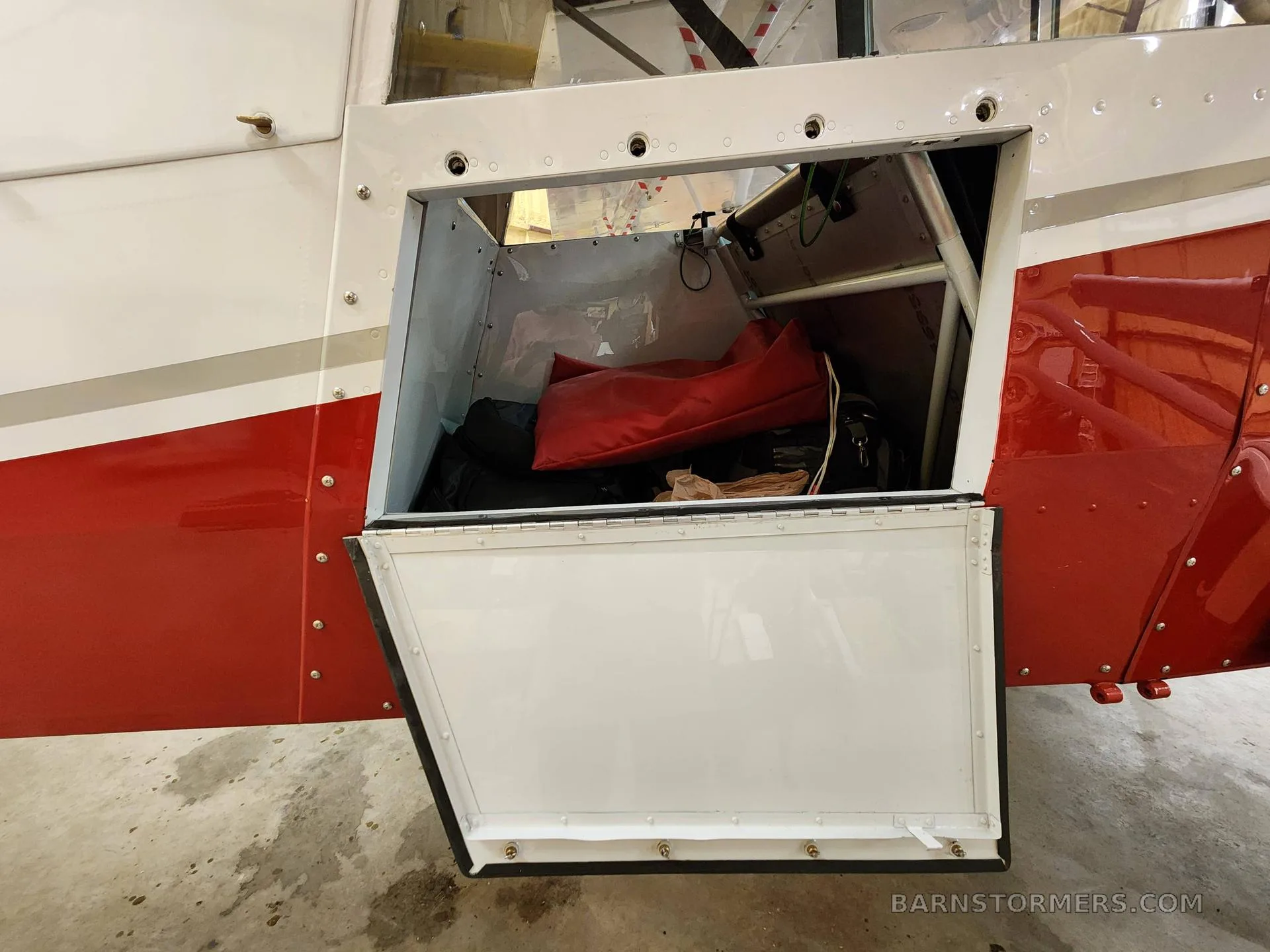 An open cargo compartment on the side of a red and white aircraft, revealing a red bag and other items inside.