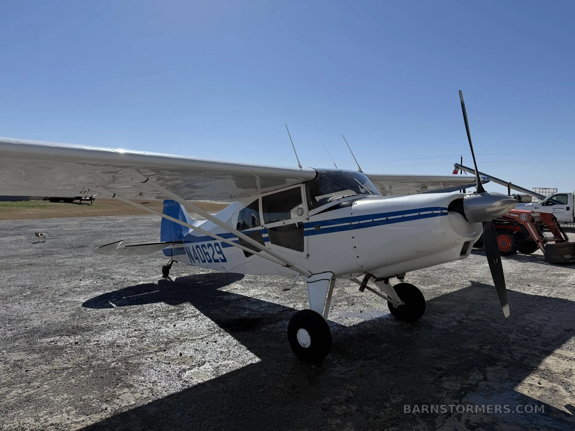 A white and blue Maule aircraft (N40629) with a propeller, parked on a gravel surface, viewed from the front-right.
