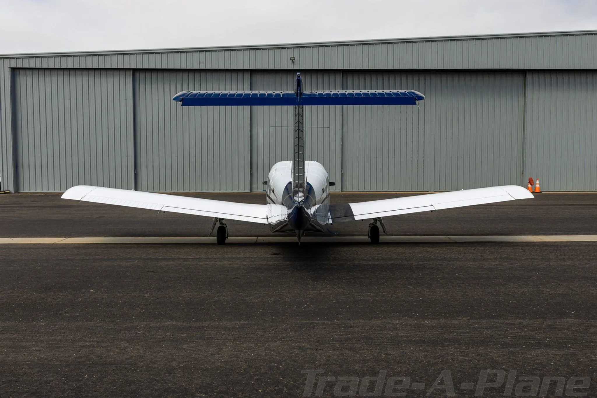 A rear view of the white and blue Piper aircraft N318PK parked on an airport tarmac in front of a hangar.