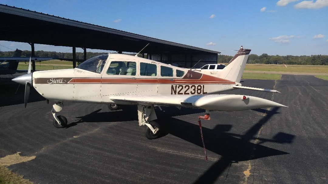 A white and brown single-engine aircraft, N2238L, parked under a hangar on an airfield.