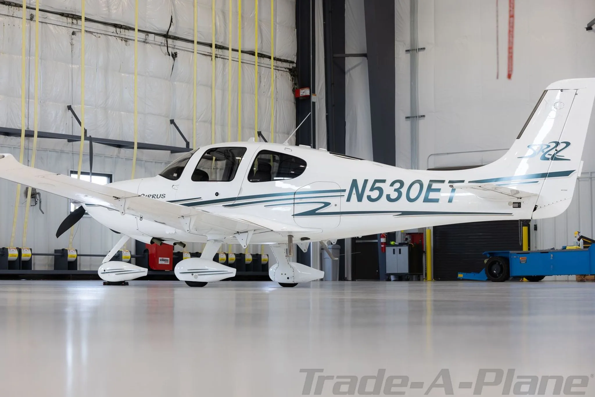 A white Cirrus SR22 aircraft with N530ET registration and green stripes is parked in a hangar, viewed from the right side.