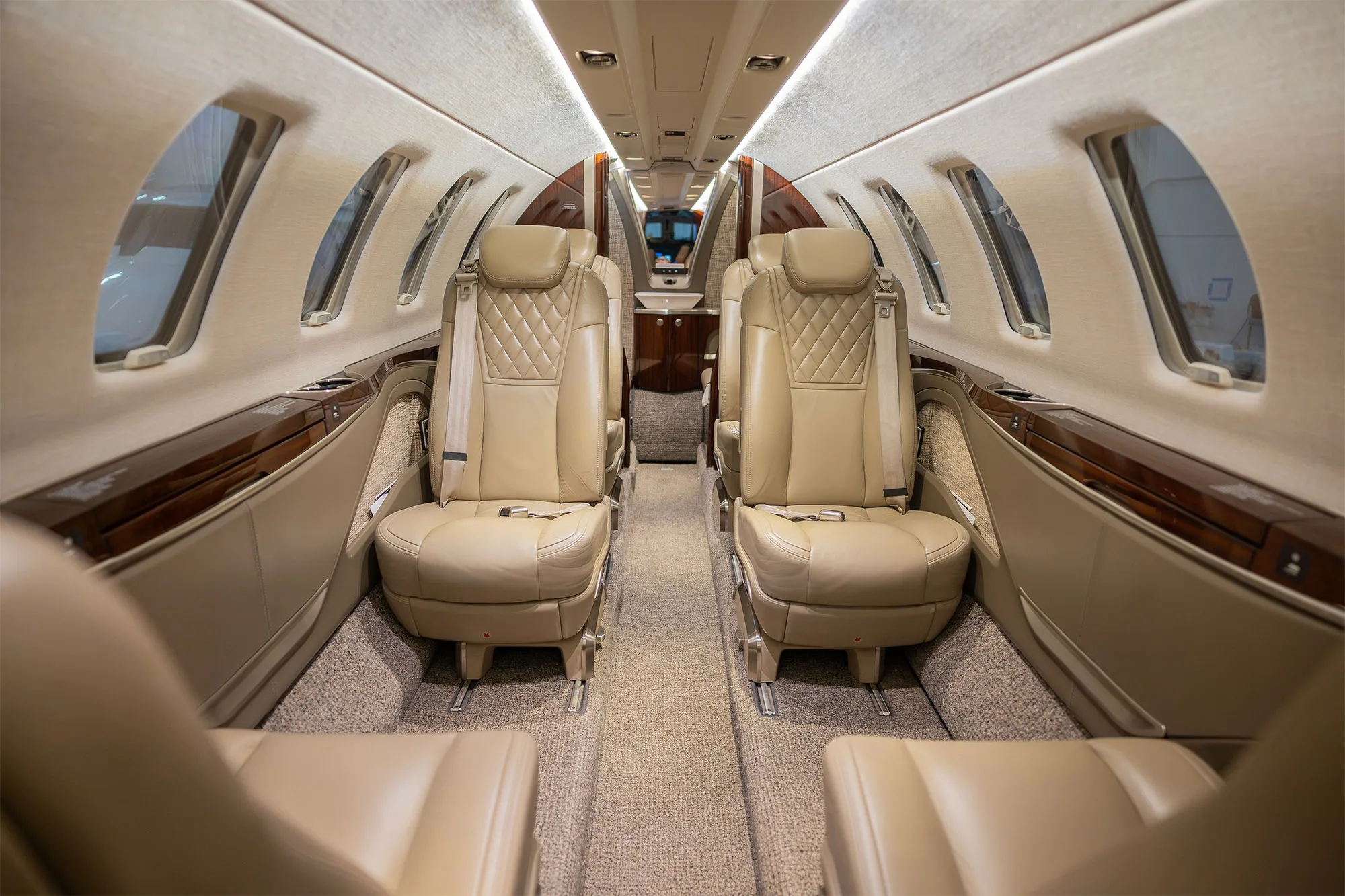 The elegant interior cabin of a business jet with beige quilted leather seats and wood paneling.