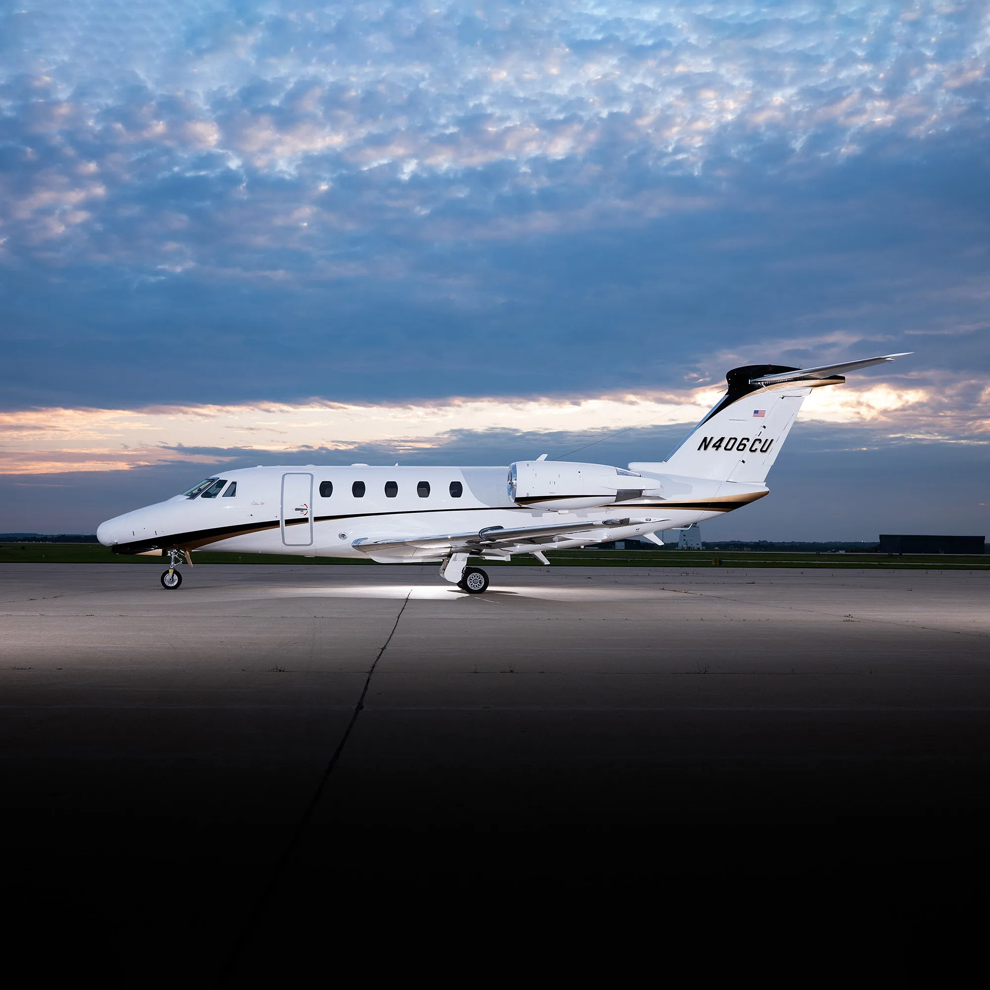 A white and black business jet (Cessna Citation) with registration N406CU parked on a tarmac at sunset.