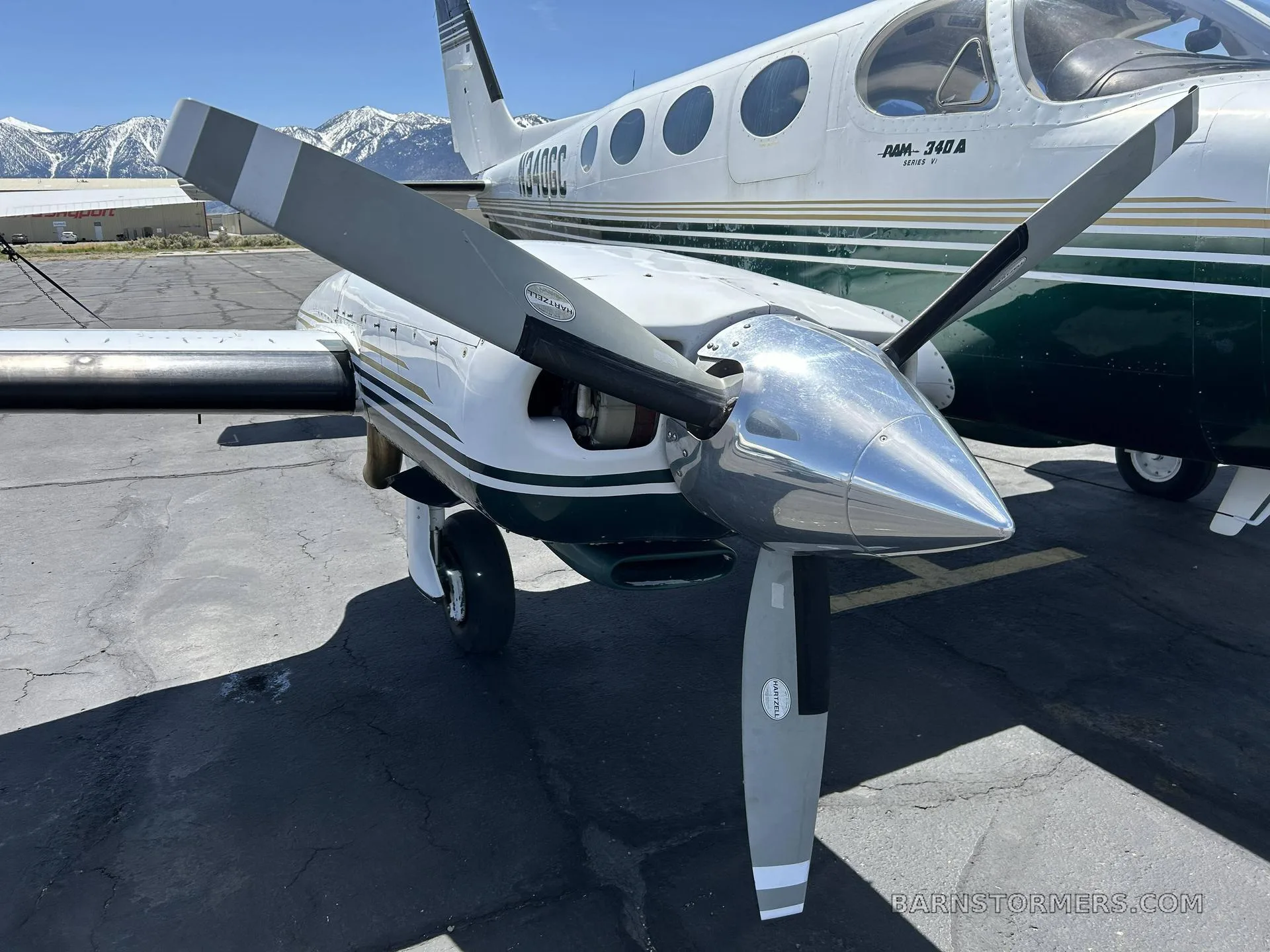 A close-up view of the right propeller and nose of a white and dark green Cessna RAM-340A Series II aircraft, with mountains in the background.