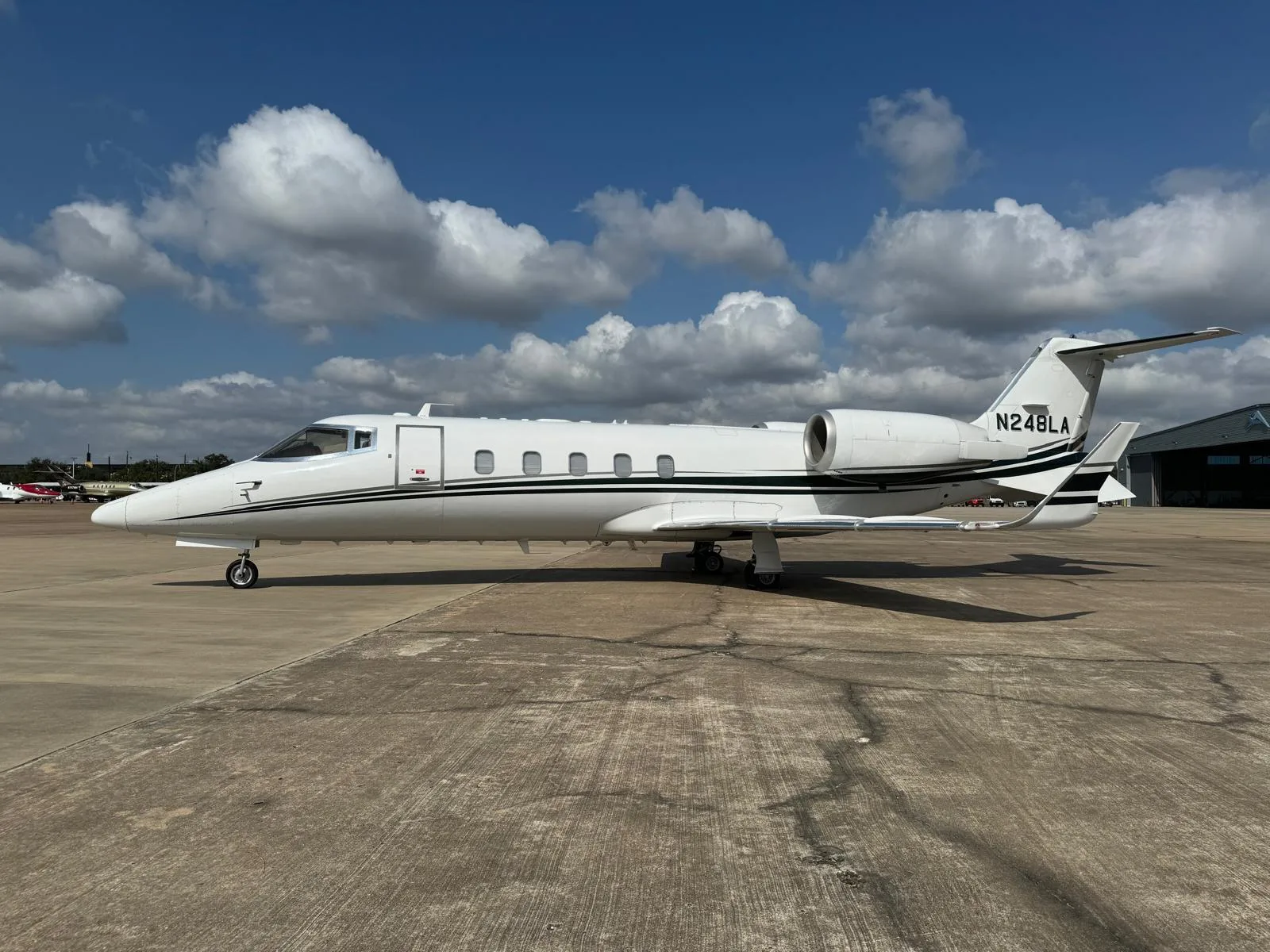 A white private jet with black and green stripe livery, registration N248LA, parked on an asphalt tarmac under a partly cloudy sky.