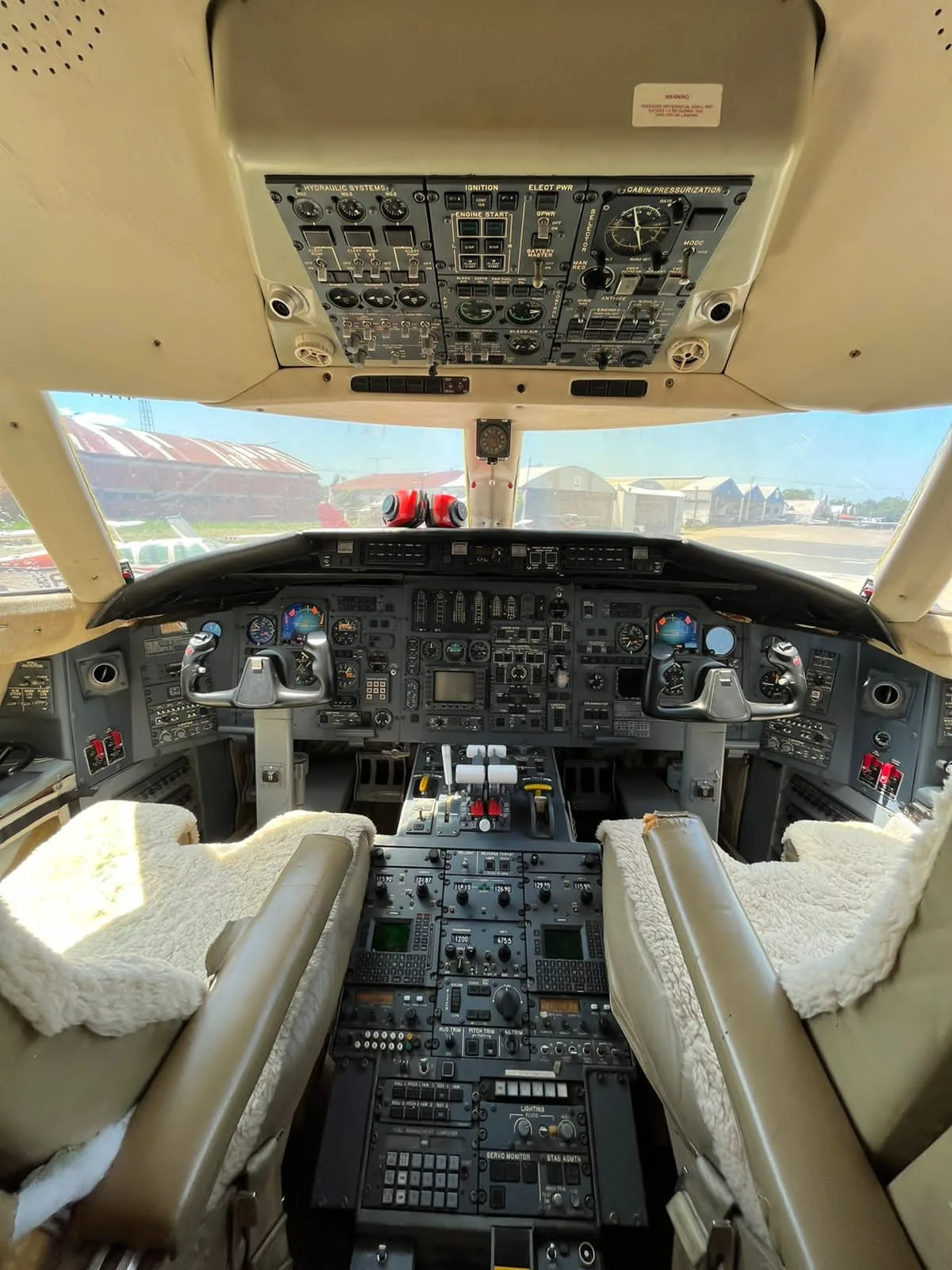 The cockpit of a business jet, showing the instrument panel, yokes, and overhead controls, with sheepskin seat covers.
