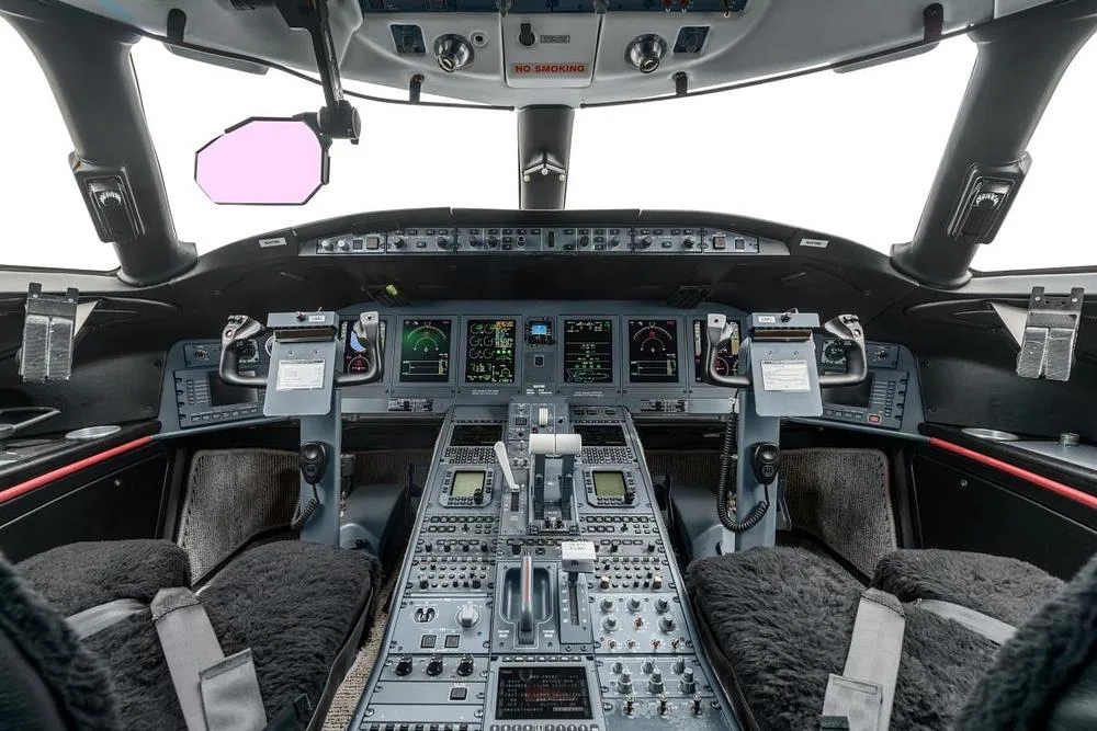 The cockpit of a Bombardier Global 7500 features multiple digital displays, control panels, and two sheepskin-covered pilot seats.