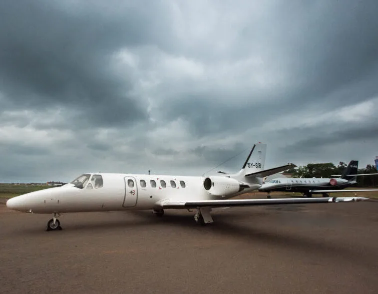 A white Cessna Citation business jet with registration 5Y-SIR parked on a tarmac under a cloudy sky, with another jet in the background.