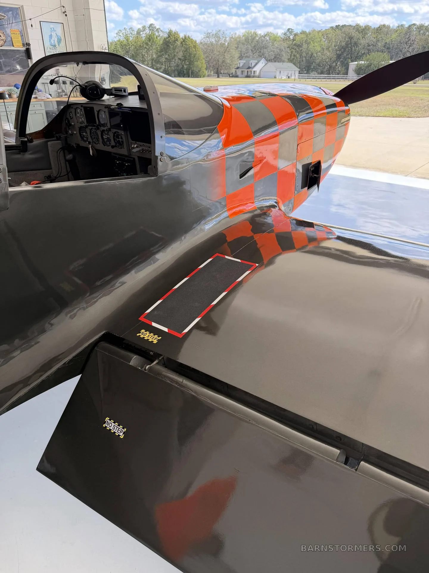 A close-up view of the black and orange checkered nose and cockpit area of a single-engine aircraft.