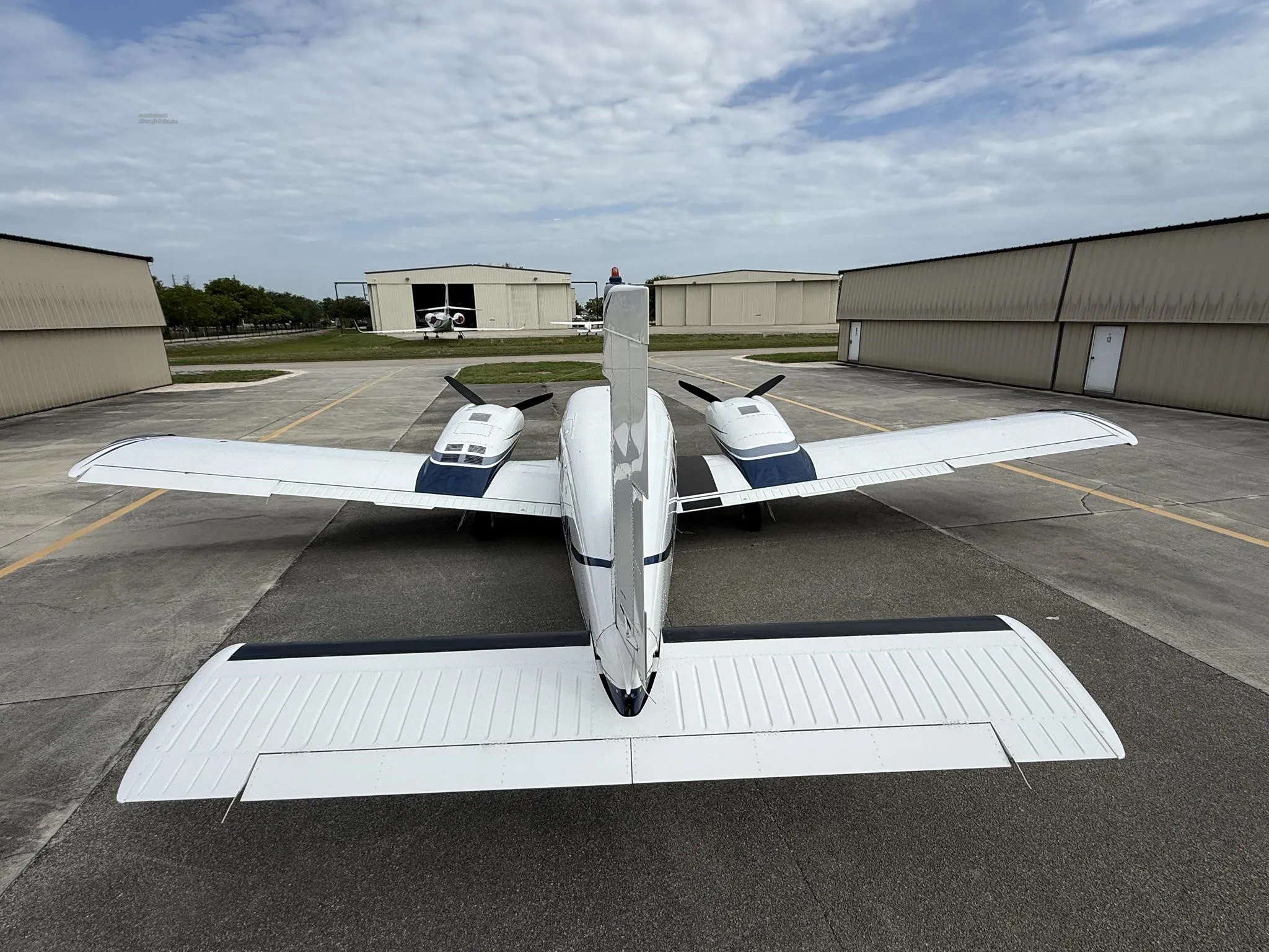 A rear view of a white and blue Piper Seneca V aircraft parked on an airfield tarmac.