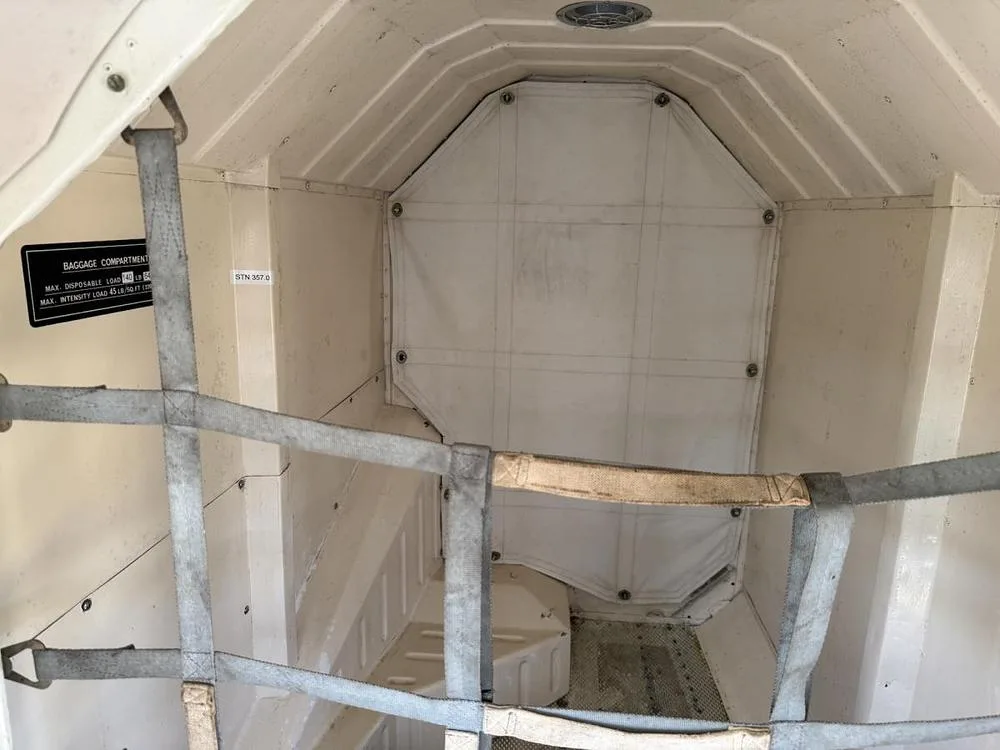 An empty aircraft baggage compartment with a cargo net and a weight limit label.