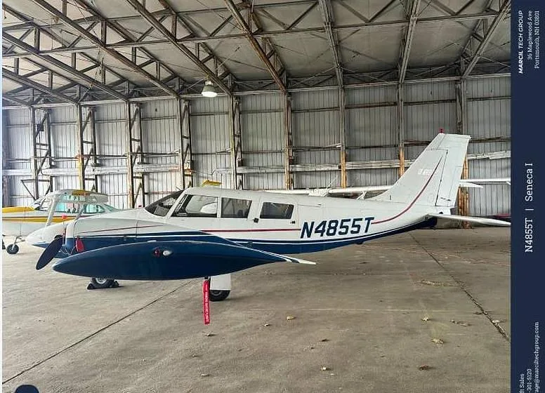 A white and blue Piper Seneca I aircraft with registration N4855T is parked inside a hangar.