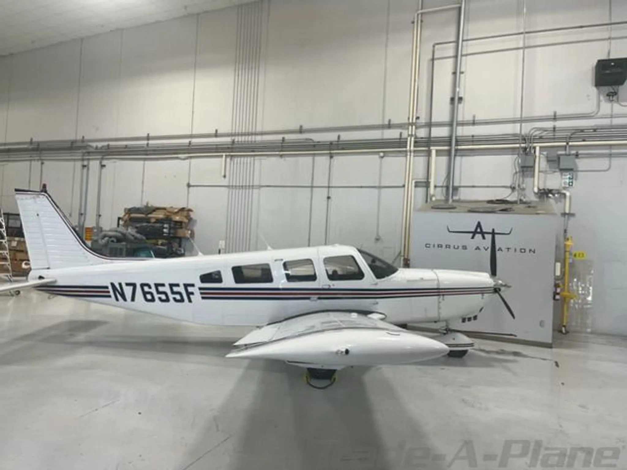 A white single-engine propeller aircraft with N7655F registration and red and black stripes is parked in a hangar.