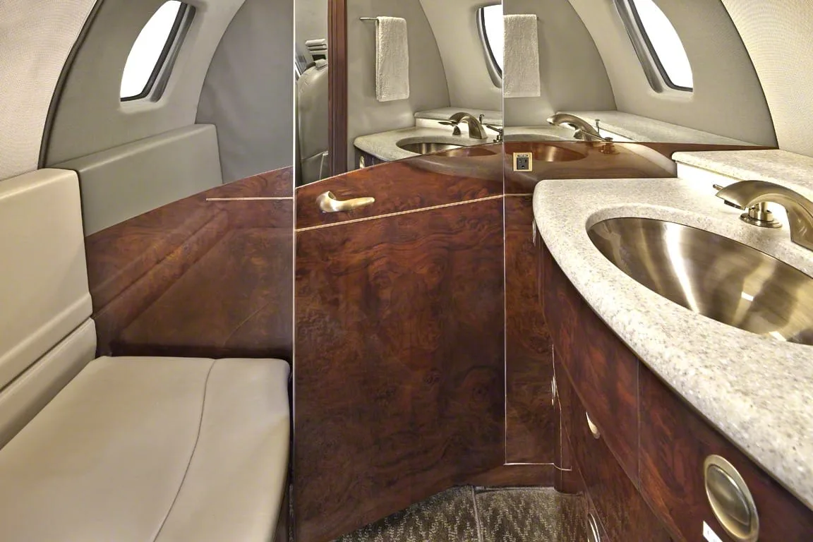 A private jet lavatory with a granite countertop, stainless steel sink, and dark wood cabinetry.