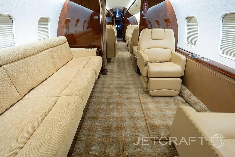 The private jet cabin interior featuring a long beige sofa and individual beige leather seats.