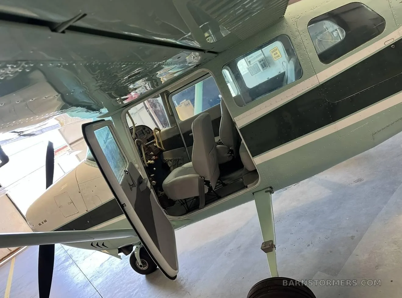 A light green and dark green Cessna 210 with its door open, parked inside a hangar.