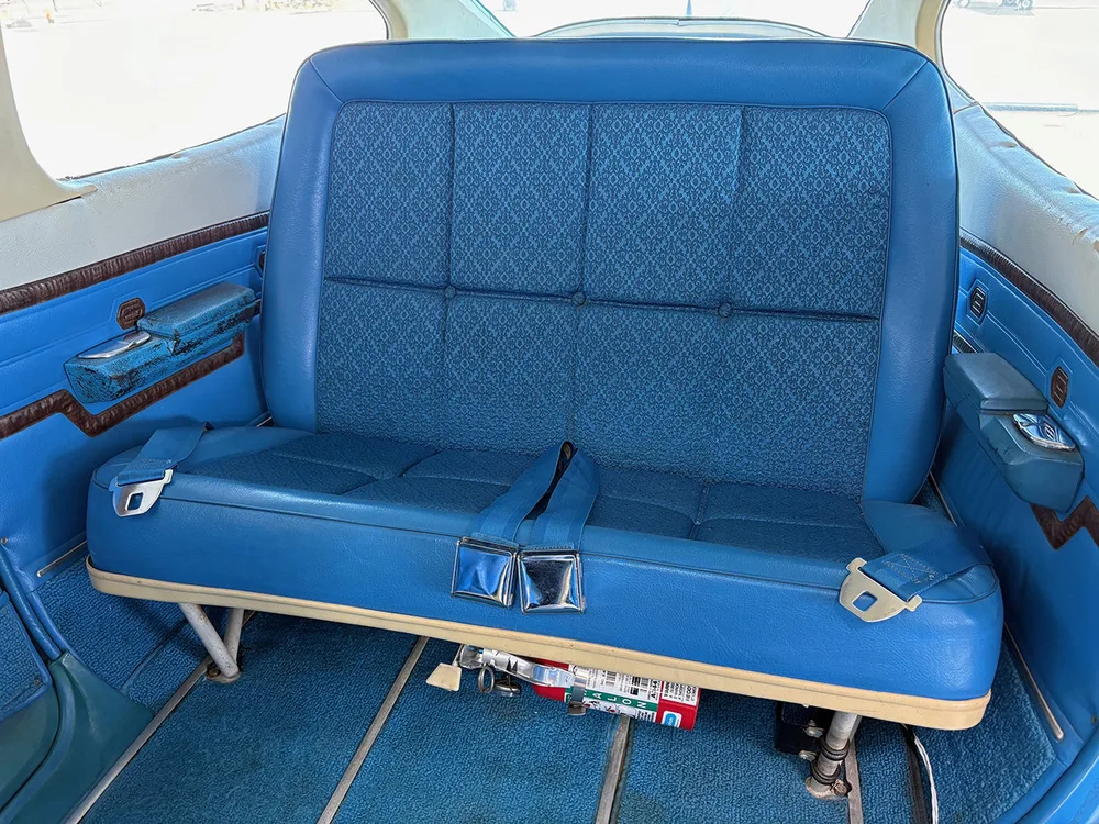 The blue rear bench seat of a Cessna 177 aircraft cabin, with a fire extinguisher visible underneath.