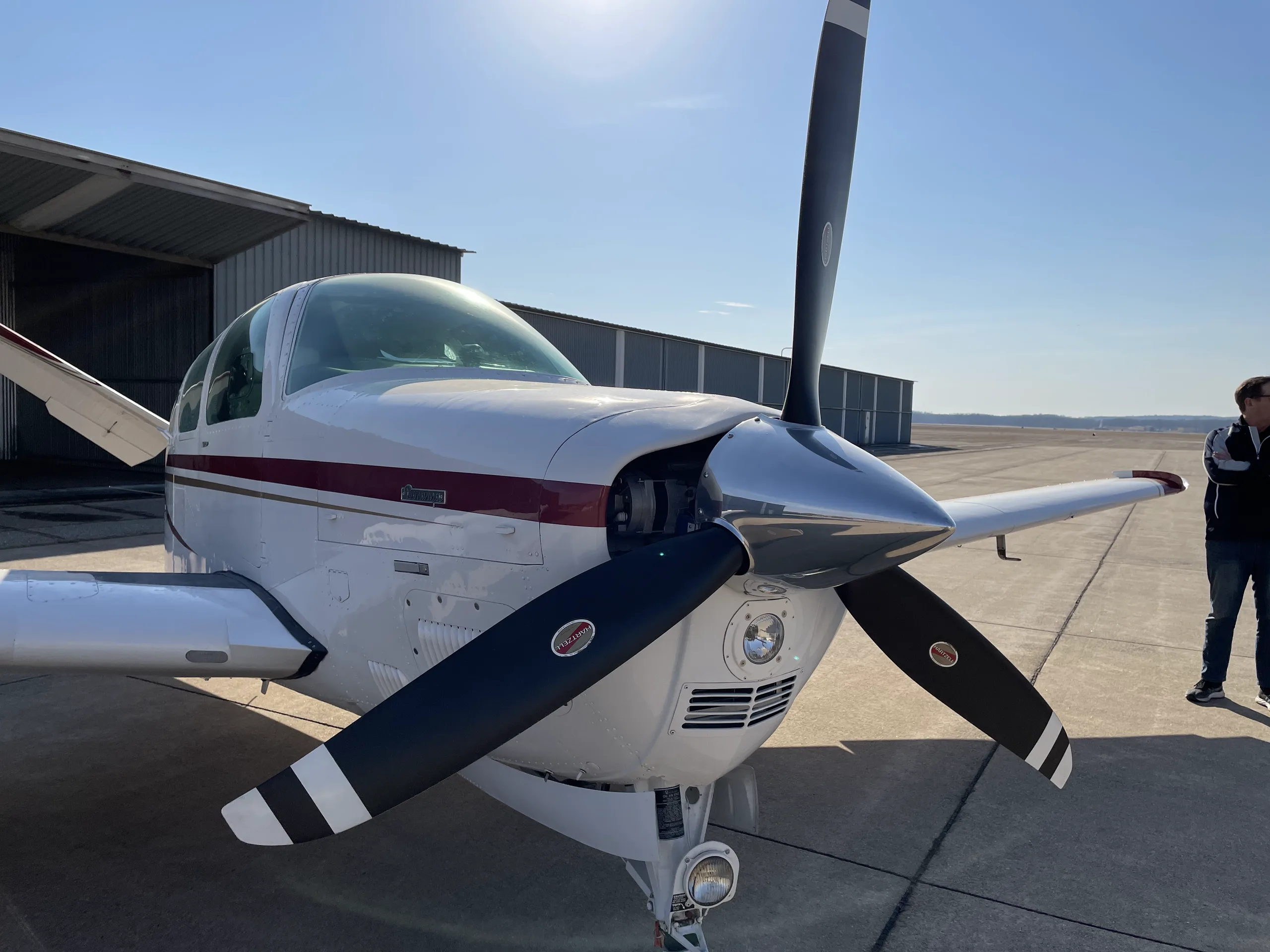 Front view of a white propeller aircraft with red and gold stripes, parked on an airfield.