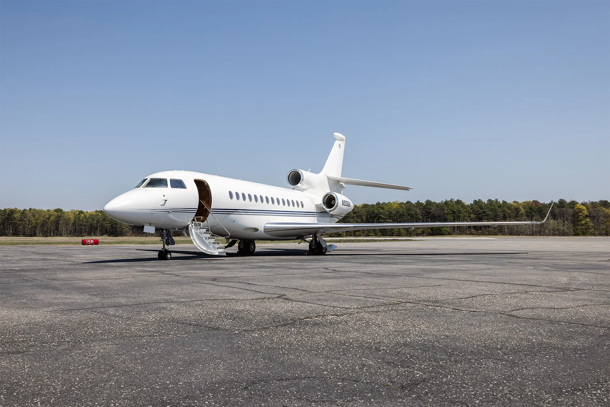 A white Dassault Falcon 900EX business jet with its main entry door open and stairs extended, parked on an asphalt tarmac.
