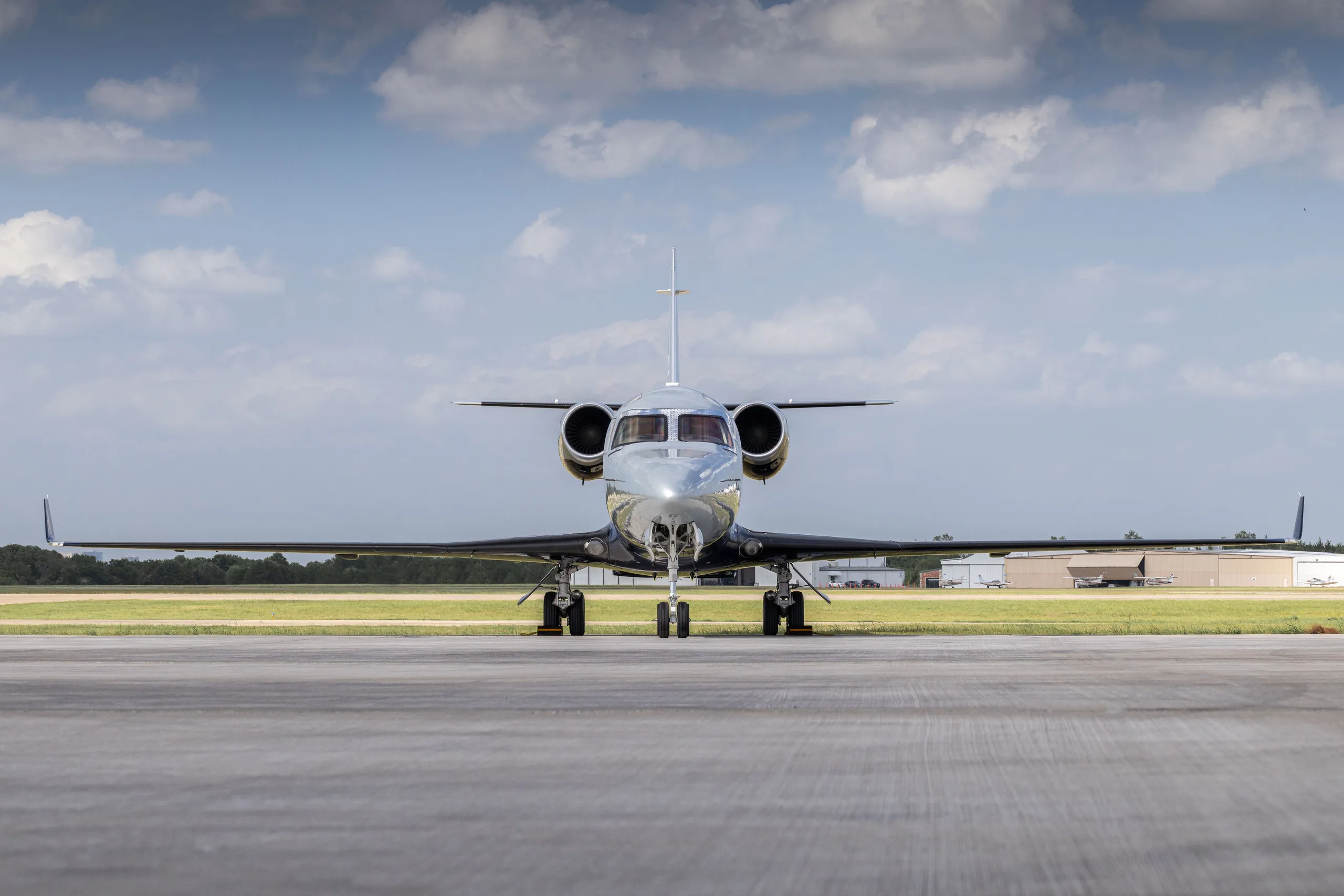 A head-on view of a Learjet 60 in a grey and dark blue paint scheme, parked on an airport tarmac.