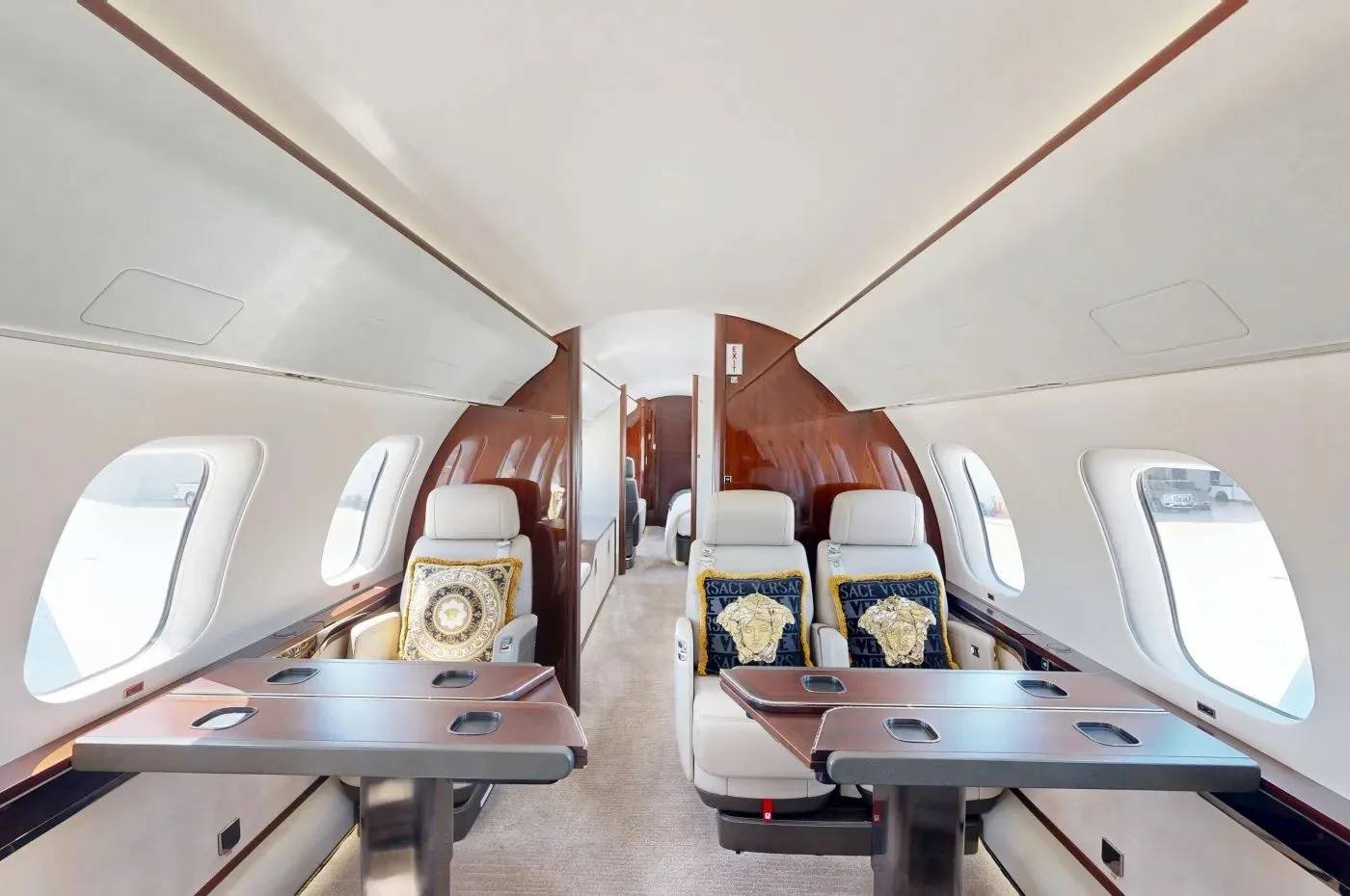 The forward cabin of a private jet with two sets of facing cream leather seats and fold-out tables.